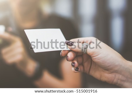 Closeup of instant photo in woman's fingers. Blank white business card in female's hand. Ring on finger. In background is blurred woman holding an instant camera. Film effect,blurred background.
