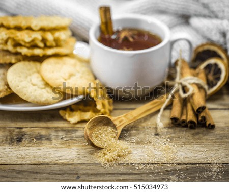 delicious cookies and a Cup of hot tea with a cinnamon stick and a spoonful of brown sugar on wooden background, holiday concept and warm mood