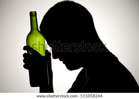 Silhouette of a man drinking wine from the bottle and smoking.  Alcohol and substance abuse concept Royalty-Free Stock Photo #515058244