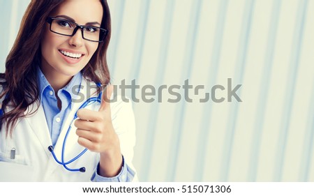 Happy smiling female doctor in glasses, showing thumbs up hand sign gesture, at office, with blank copyspace area for slogan or advertise text. Healthcare, medical, lab consulting and exam concept.