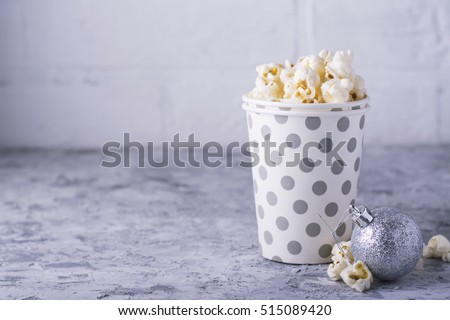 Salty fresh crusty homemade popcorn in silver paper cup in the fashion light background of white brick wall in a New Year's interior with silver Christmas balls. selective focus
