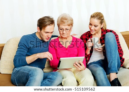Young couple with old woman sitting on couch and watching something on tablet