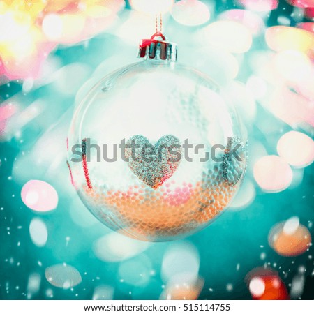 Hanging Christmas ball from glass with heart symbol  on blue bokeh background with snow