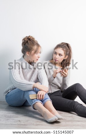 portrait two surprised girls looking at cell phone discussing latest gossip news, shopping, shocked at what they see, isolated white background