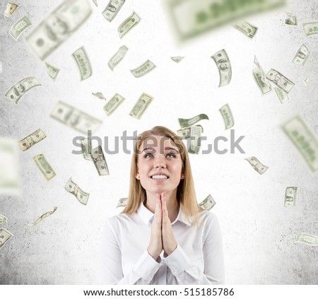Beautiful blond businesswoman is standing under dollar rain and praying for it never stop. Concept of suddenly becoming rich