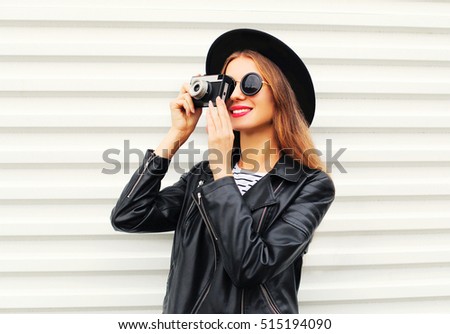 Fashion look, pretty young woman model with retro film camera wearing elegant hat, leather rock jacket over white background