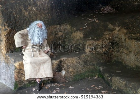 Thinking hermit sitting at the rocky seat in cave. The bearded philosopher in a stone shelter.