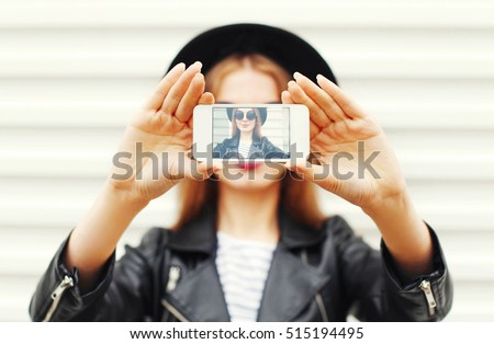 Fashion cool girl taking picture self portrait on smartphone over white background