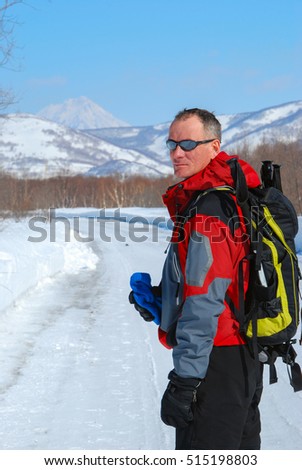 Hiker walks along the road in winter forest, on the background of snow covered hills and volcano.
