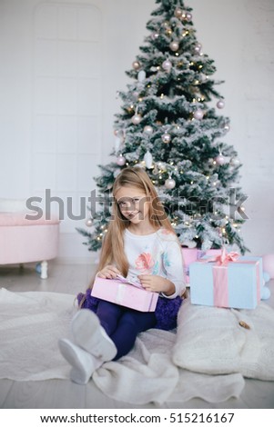 girl holding a gift box near the Christmas tree. Blond hair kid opening Xmas present