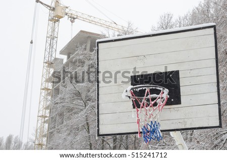 Snow-covered basketball hoop with industrial background. torn mesh basketball hoop