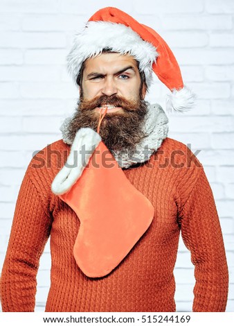 young handsome bearded santa claus man with long beard in red sweater and new year hat holds decorative christmas or xmas stocking or boot on white brick wall background