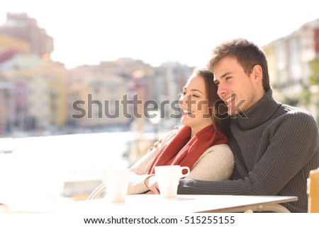 Couple relaxing sitting in an hotel terrace on holidays with a port in the background in a sunny day of winter