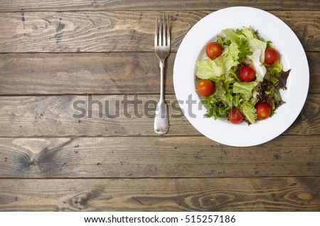 A bowl of fresh garden salad on a rustic wooden dining table background with fork and blank space at side