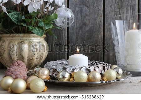 Christmas decoration with round wreath, glass golden mini balls, lit candle on vintage metal silver plate, candle in glass candlestick, pattern snowflakes, cone, fresh withe cyclamens in ceramic pot