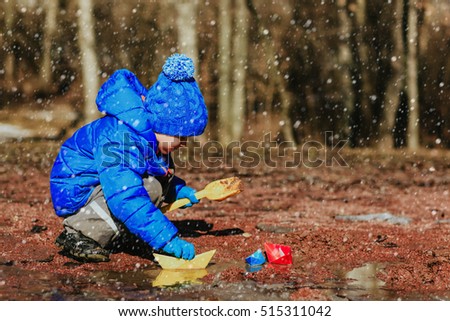 little boy plaing with paper boats in winter