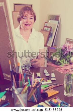 Happy smiling mature woman painting for fun with paints at home
