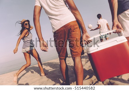 Friends on the beach. Rear view of cheerful young people walking by the beach to the sea while two men carrying plastic cooler Royalty-Free Stock Photo #515440582