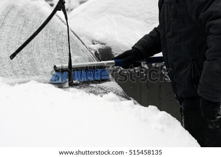 Winter, snow, car winter problems. Visible hand of a man in a black jacket and glove, which cleans the car from snow with the help of special brushes.