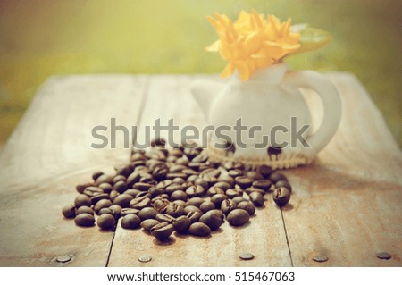 Heap of roasted coffee beans isolated on grunge wood background with Ixora flower pot, morning light and garden view