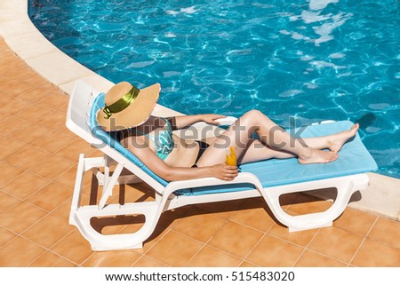 Pretty woman in hat relaxing on sun lounger in the edge of swimming pool 