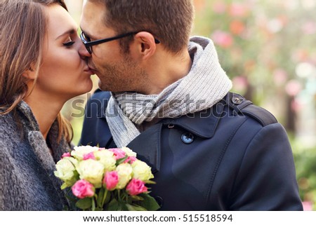 Picture showing young couple with flowers kissing in the park