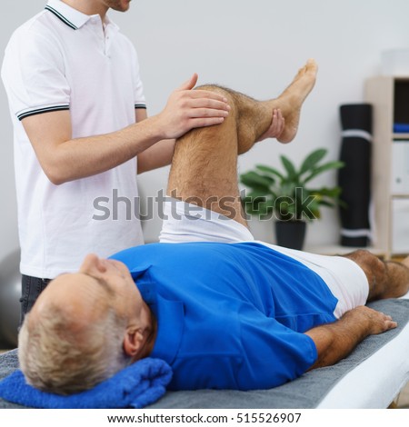 Physiotherapist flexing an elderly male patients knee as he performs an examination or mobility exercise