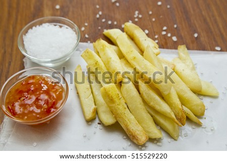 Tasty baked French fries on grease proof paper with salt and ketchup sauces Royalty-Free Stock Photo #515529220
