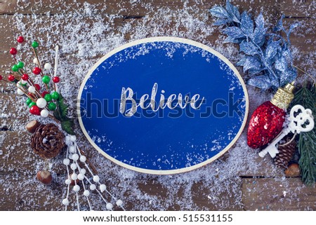 Believe Written In Chalk On Blue Chalkboard Holiday Sign Background With Snow And Decorations. Top View.