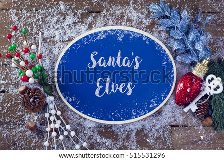 Santa's Elves Written In Chalk On Blue Chalkboard Holiday Sign Background With Snow And Decorations. Top View.
