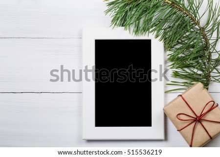 Photo frame with gift box on wood background. Decorated pine branches. Top view