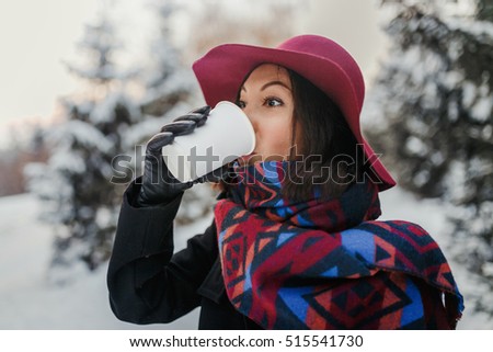 Stylish beautiful young woman drinks tea on winter nature background outdoor