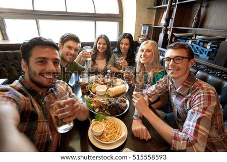people, leisure, friendship and technology concept - happy friends taking selfie, drinking beer and eating snacks at bar or pub