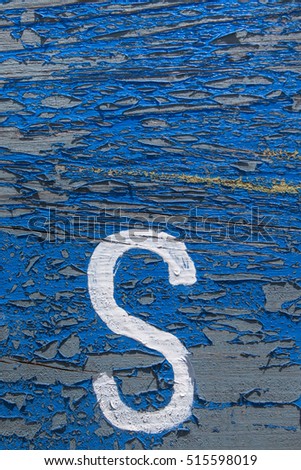 Blue texture of peeled paint on wood with a S letter painted in white.