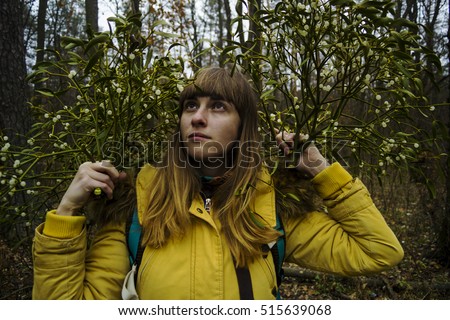 Young beautiful brown-haired ethnic girl like a witch, with long hair, looks like a dryad, holding sprigs of mistletoe in the autumn forest. Divination