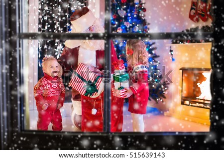 Children and Santa Claus at fireplace on Christmas eve. Family celebrating Xmas. Decorated living room with tree, gifts, fire place, candles. Winter evening at home for parents and kids.
