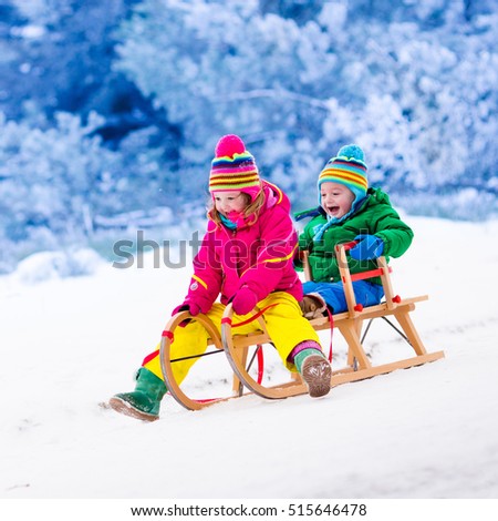Little girl and boy enjoy a sleigh ride. Child sledding. Toddler kid riding a sledge. Children play outdoors in snow. Kids sled in Alps mountains in winter. Outdoor fun for family Christmas vacation.