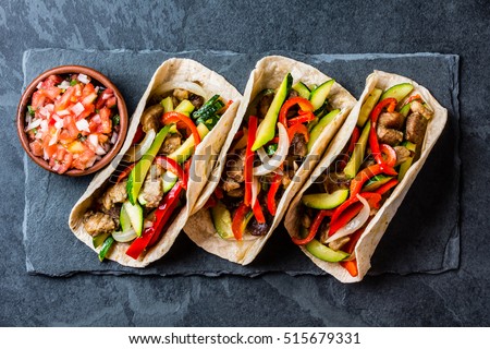 Mexican pork tacos with vegetables and salsa. Tacos al pastor on black stone slate plate on black background. Top view
