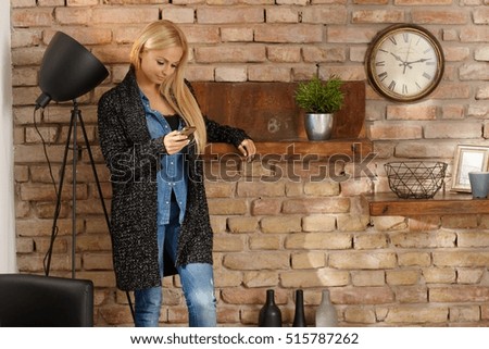 Young woman in retro home standing by brick wall, using mobilephone.
