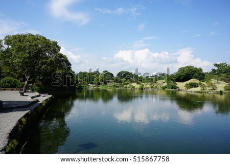 A Japanese garden with grass, trees and lake.