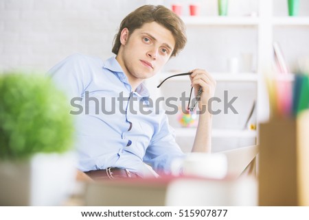 Portrait of attractive european boy at modern workplace with laptop, supplies and other items