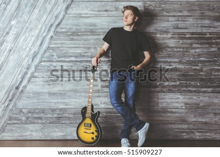 Attractive european boy with electric sunburst guitar in wooden room. Music concept