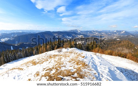 A hill covered in snow and frozen earth on the background of the Carpathian mountain range. Sunny frosty day; several clouds in the blue sky