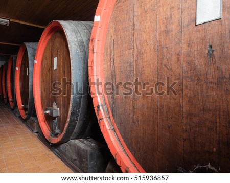 Picture of a brown wine barrels stacked in the old cellar of the winery. Background of the wooden barrels made of brown planking.