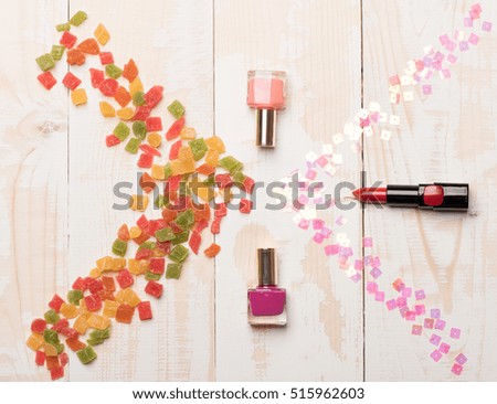 Red lipstick, bottles with nail polish and mix of marmalade or jelly candies with sequins on vintage wooden background, children`s cosmetic