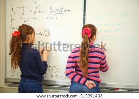 Schoolgirls write on blackboard with geometry examples and exercises in classroom, back view, text - formula, focus on text