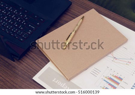 Document paper chart and black laptop with blank brown book on desk. Reports work data analysis in office