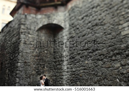 Blurred picture of wedding couple kissing under grey wall