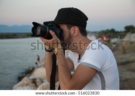 Young man Photographer is taking a still image near the sea in the Afternoon. Side view.