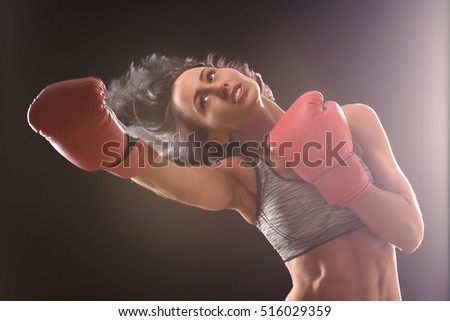 Boxing concept. Brunette woman with red lips making direct his during fight or battle over black background in studio.